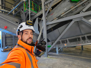 Homme en tenue de travail et casque, appareil photo à la main dans une usine