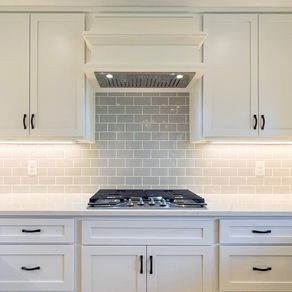 Cooking and baking zone design with stainless steel wall ovens, gas cooktop, white cabinetry, and under-cabinet lighting in a modern kitchen.