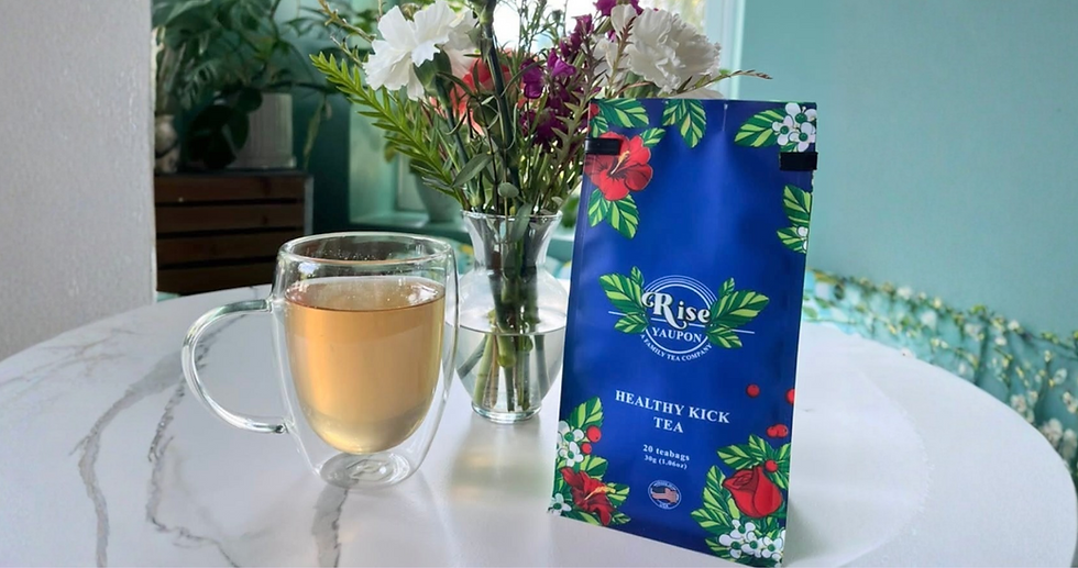 Clear tea mug beside vase of white and purple flowers and a blue Rise yaupon Healthy Kick Tea box on a bright tabletop.