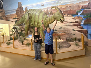 brother and sister standing in front of dinosaur exhibit