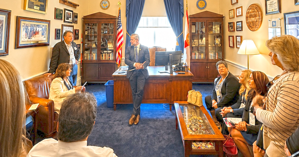 Group poses with Rep. Webster Barnaby in a government office; flags and a One Nation Under God plaque behind his desk
