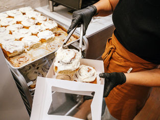woman in industrial kitchen placing cinnamon rolls into bakery box