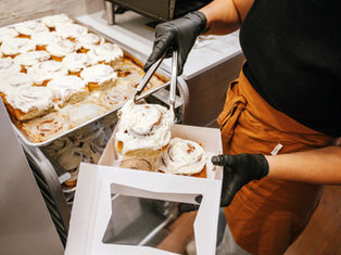 woman in industrial kitchen placing cinnamon rolls into bakery box