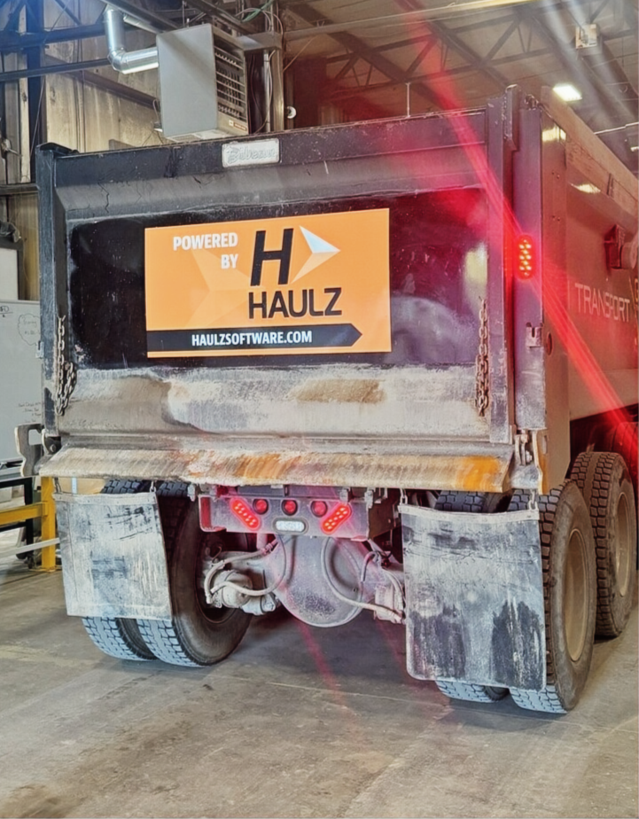 Dump truck in garage with POWERED BY HAULZ decal on back end of bed
