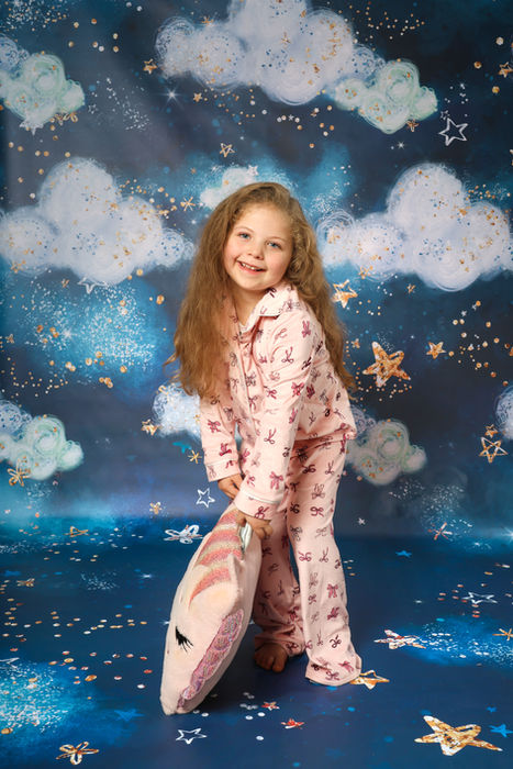Mädchen im rosa Schlafanzug lacht auf blauer Wolkenkulisse – lokale Kinderfotografie Kassel