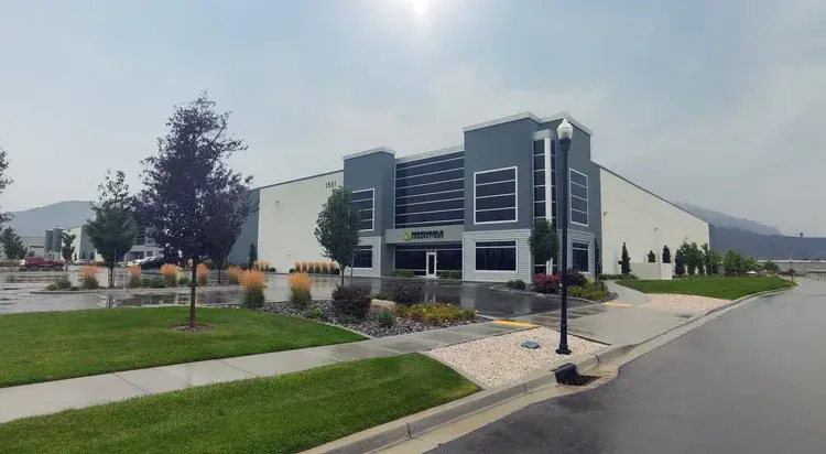 Renewable Innovations production and manufacturing center in American Fork, Utah, featuring a multi-story gray commercial office entrance with corporate signage, expansive warehouse walls, and landscaped curb areas.