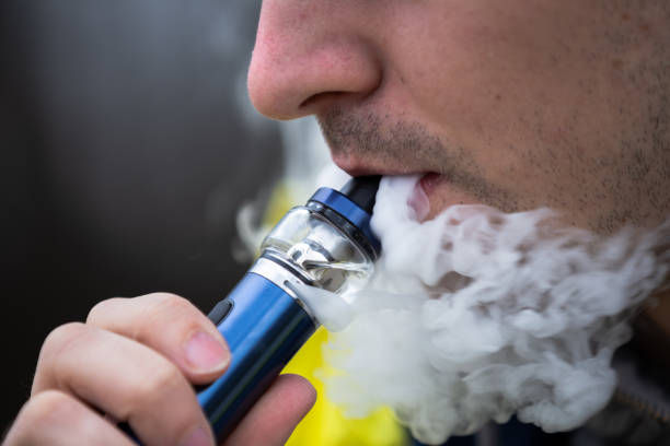 Close-up of a person vaping an e-cigarette with visible vapor smoke.