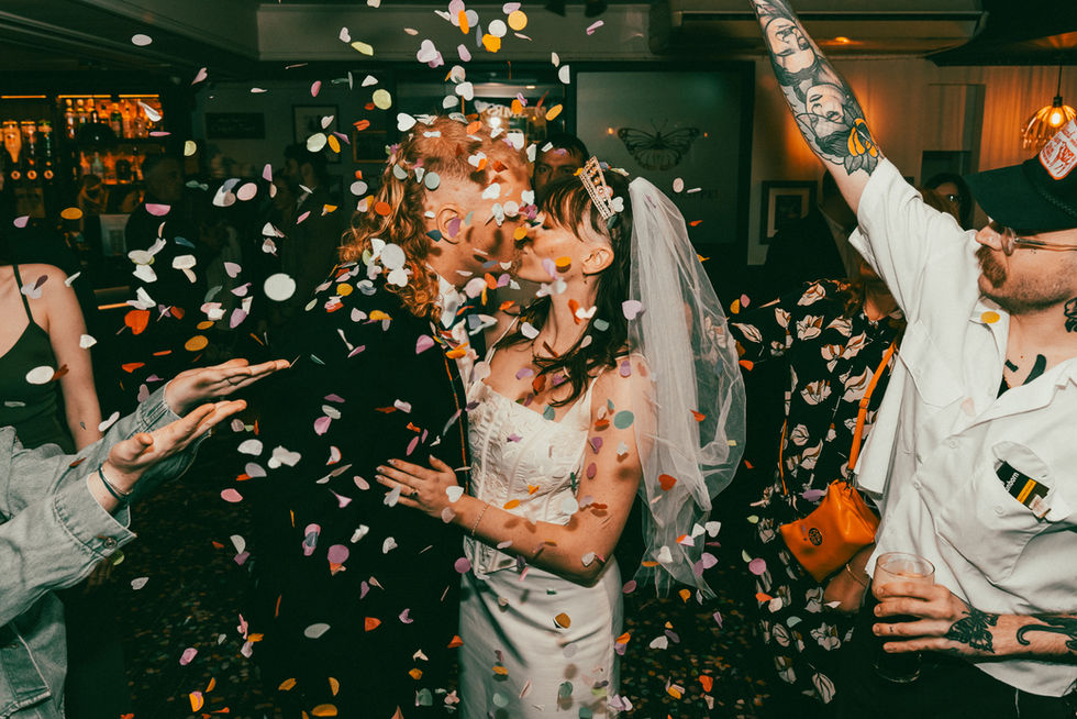 a bride and groom kiss while confetti is thrown at them