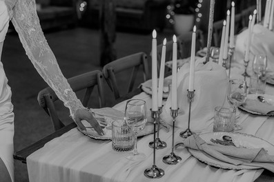 a refined cottagecore wedding reception tablescape with realistic flame imitating taper candles, gold candlestick holders, gold embossed charger plates, gold cutlery, beige knotted napkin and lace bow around gold cutlery