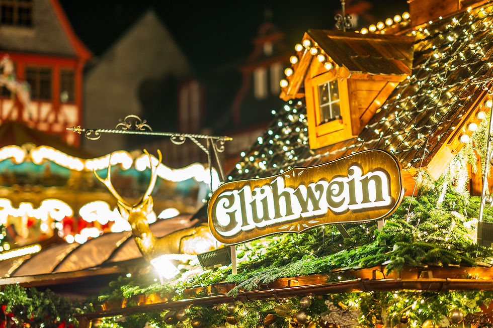Glühwein sign glowing at a festive Christmas market stall with warm lights, wooden roof, and blurred holiday buildings.