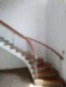 Baranda curva calandrada a medida con postes de acero inoxidable y varillas paralelas flexibles que se adaptan perfectamente a la silueta de la escalera.