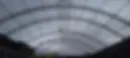 Perspectiva interior de la distribución geométrica de una cobertura parabólica metálica de gran luz. La estructura destaca por el montaje de arcos reticulados tubulares, un entramado longitudinal de correas de soporte y una sección central sobreelevada para ventilación (linternón), donde el personal técnico ejecuta soldadura de campo en altura para consolidar la rigidez del conjunto.