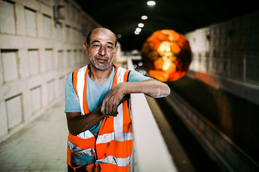 פועל בניין בתחנת רכבת חדשה, מסתכל למצלמה עם אפוד זוהר כתום