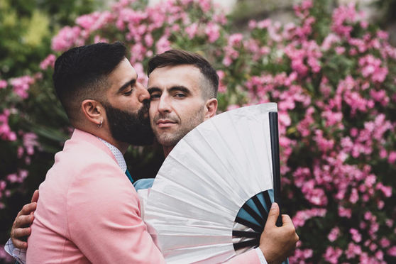 גבר מחבק גבר אחר, מאחורי פרחים ורודים עם מניפה. צילומי אירועים.