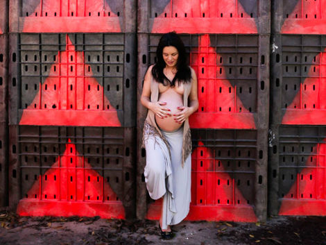 אישה הרה עומדת ליד קיר עם משולשים אדומים צילומי הריון על רקע מיוחד