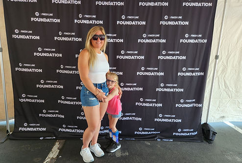 Brittany Urbanowicz and her daughter Sophie smiling together at the Indiana Special Olympics event. They are standing in front of a branded event backdrop, capturing a joyful moment of celebration and support.