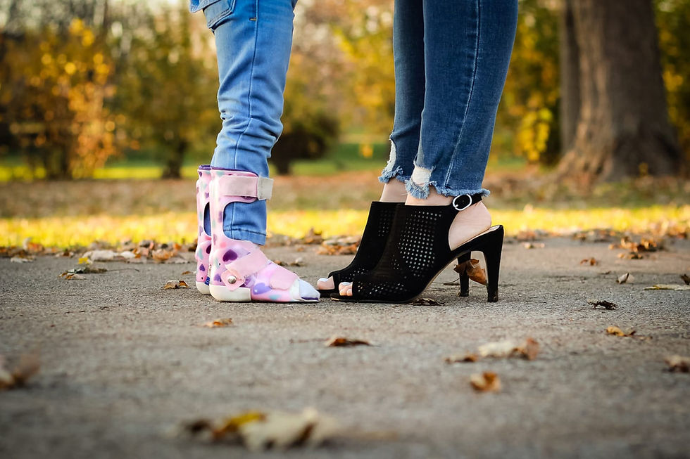 A close-up of a Sophie wearing an AFO brace on both legs, standing next to Mommy wearing black high heels, symbolizing mobility support and empowerment.