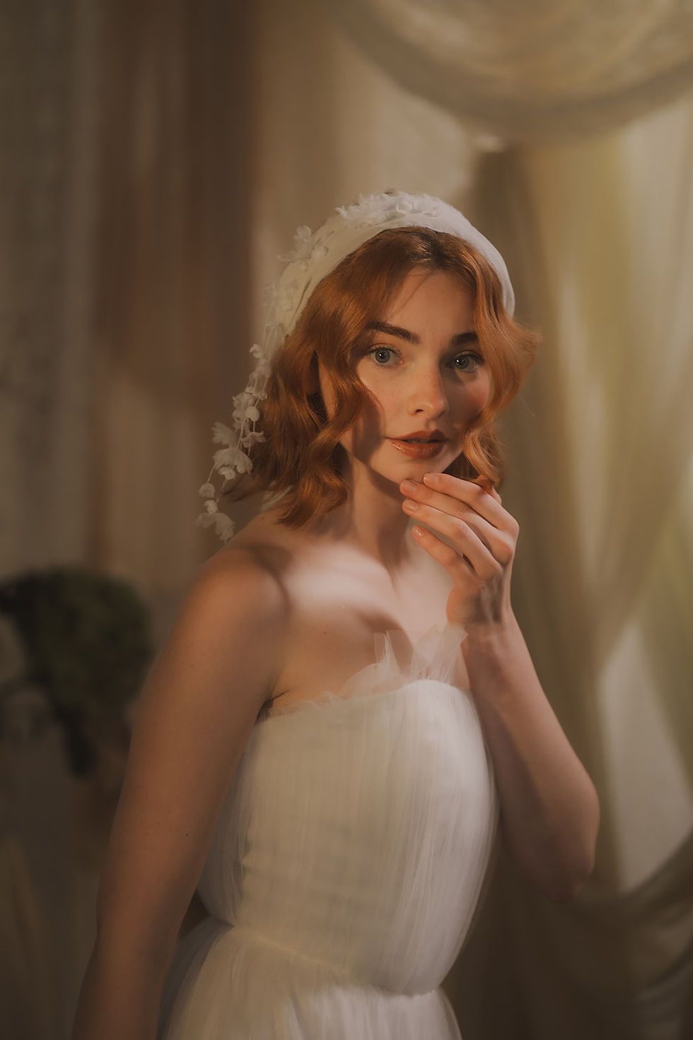 Thumbnail: Woman in white holds hair, wearing a wearing a delicate silk chiffon headband featuring delicate threads dangling down with 3D silk flowers, posing in sunlight.