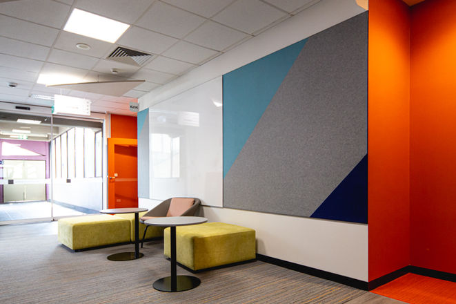 Vibrant Chisholm Institute entry corridor with geometric acoustic panels and lounge seating for informal gatherings.