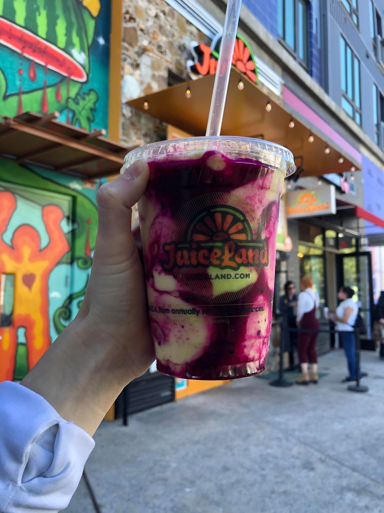 Assortment of colorful smoothies from Juiceland displayed in Lili's hand in front of the store