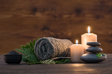 Towel on fern with candles and black hot stone on wooden background. Hot stone massage set