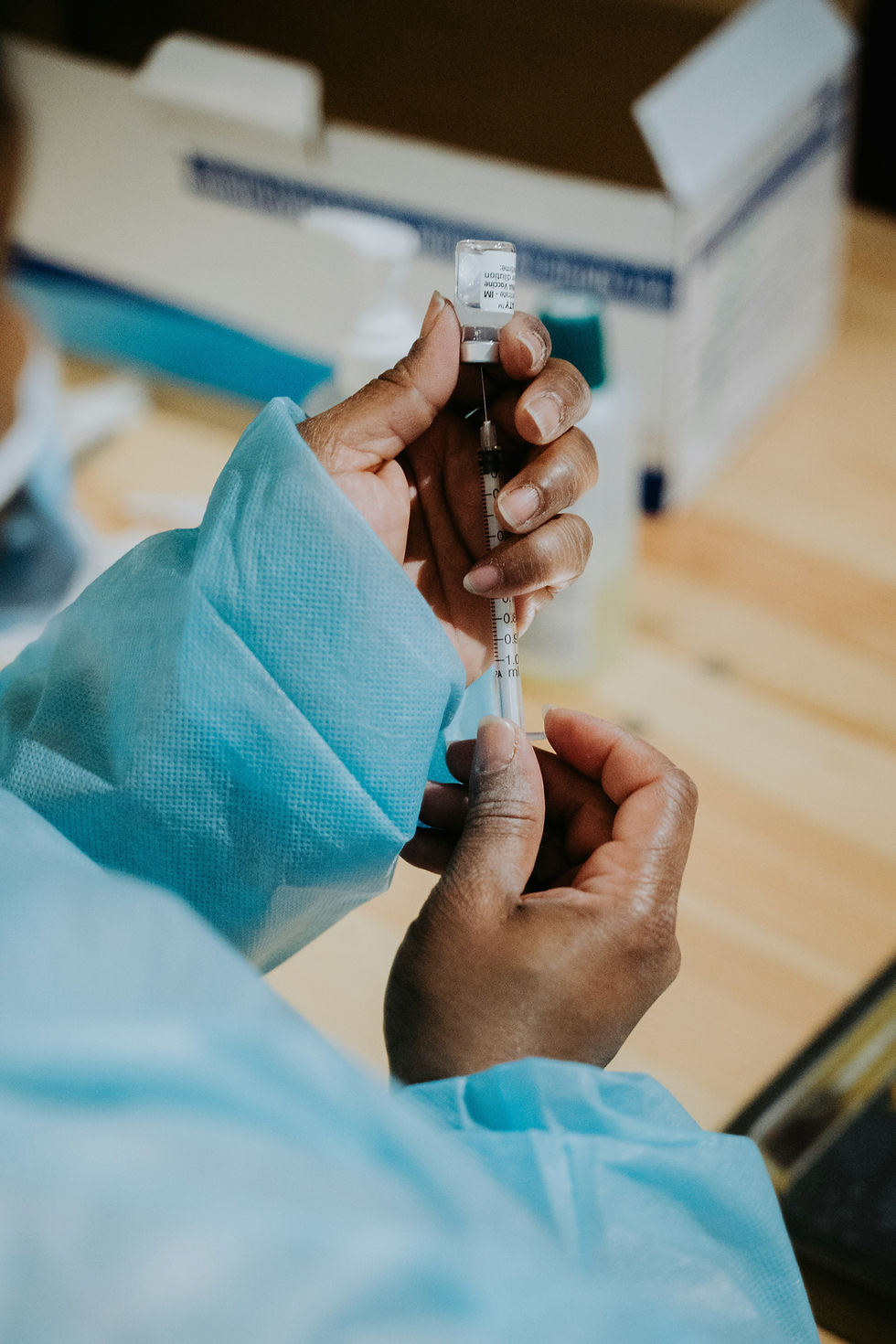 Healthcare worker in blue gown preparing a syringe and vial.