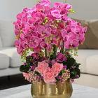 Pink orchids and roses in a gold vase on a marble table.