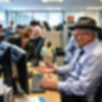 Picture of a people in office at laptop, with a man in a fedora looking at a screen while a Penguin stares at it.
