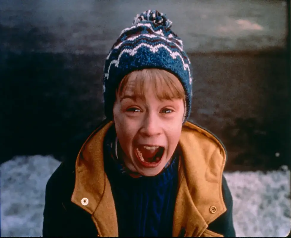 Boy wearing a blue patterned beanie and yellow coat screams joyfully outdoors. Snowy background, with an expression of excitement. Home alone, Kevin, Rockin around the christmas tree violin score for beginners