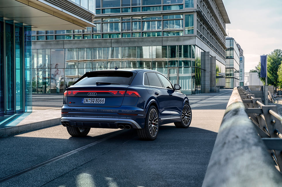 Blue car on a city road with glass buildings in the background.