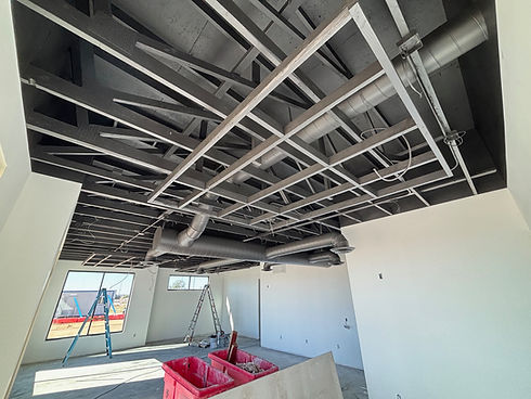 Interior exposed freshly painted ceiling construction with exposed ductwork, lighting, and freshly painted walls, construction in progress.