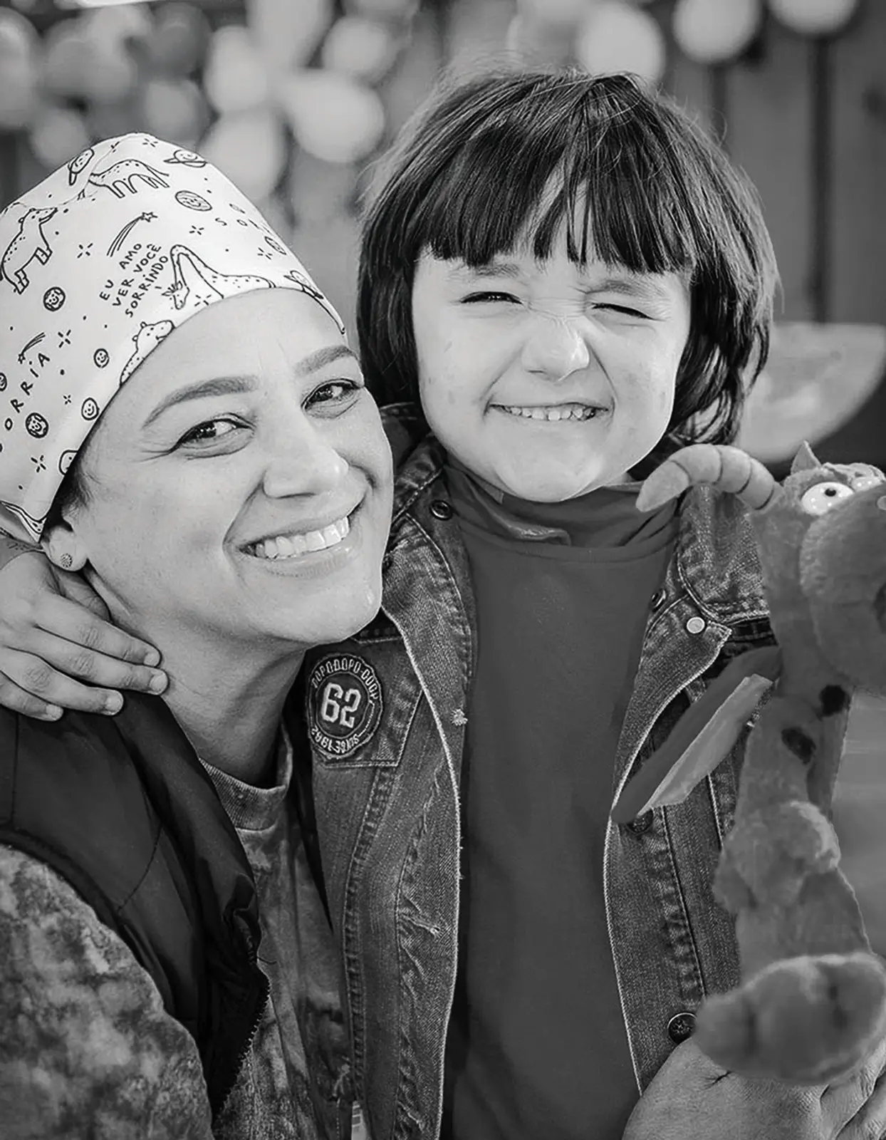 Uma voluntária e uma criança paciente piscando para a foto. As duas estão sorrindo felizes.