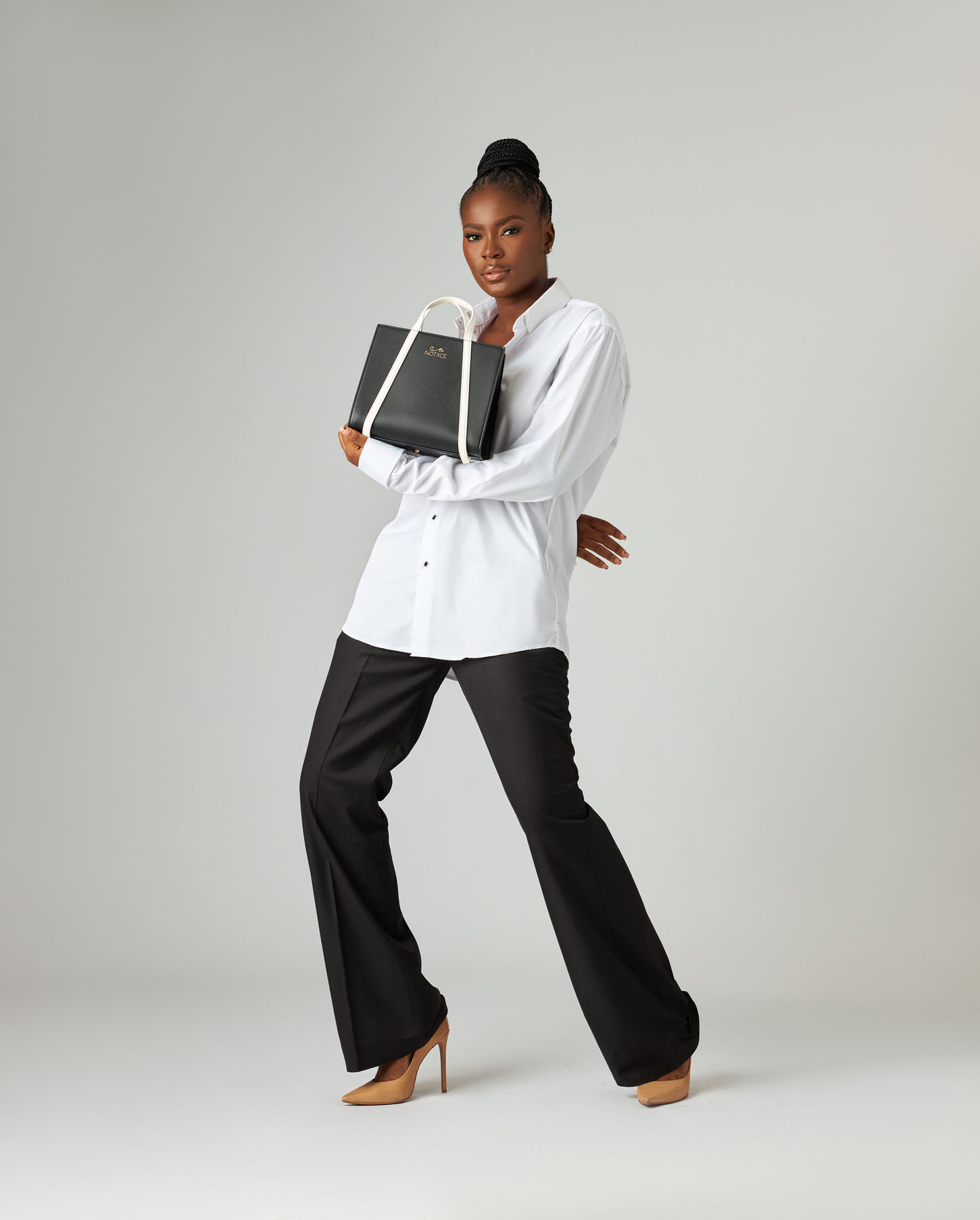 A model poses with a black tote bag in a well-lit studio setting, showcasing the bag's sleek design and spaciousness.