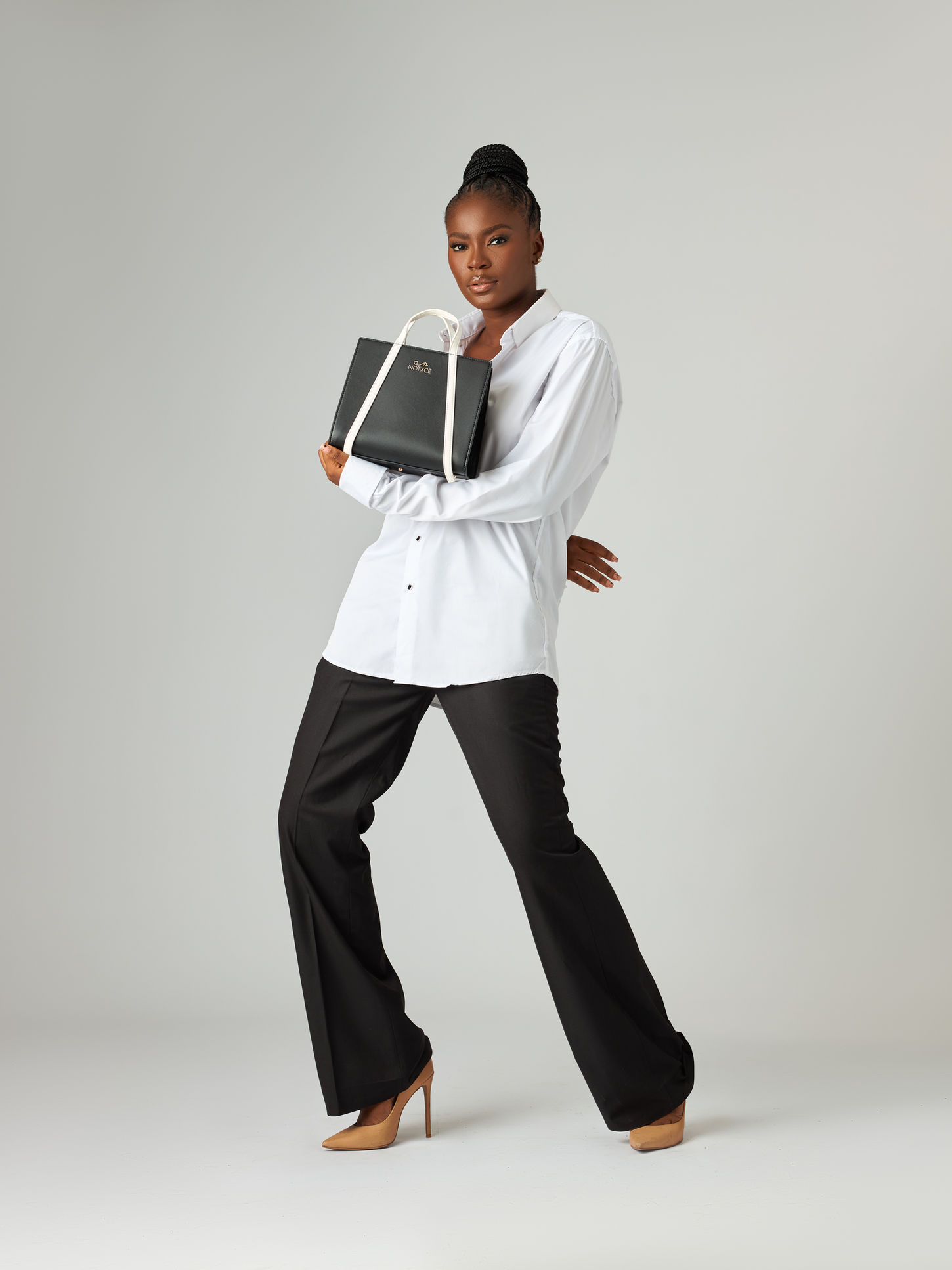 A model poses with a black tote bag in a well-lit studio setting, showcasing the bag's sleek design and spaciousness.