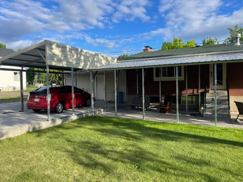 Metal roof covering a patio and parking area beside a home