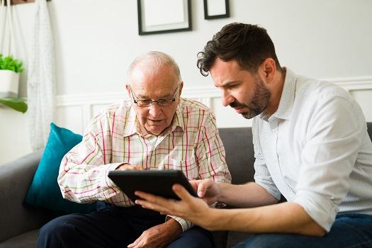 A younger man patiently helping an older man with a tablet