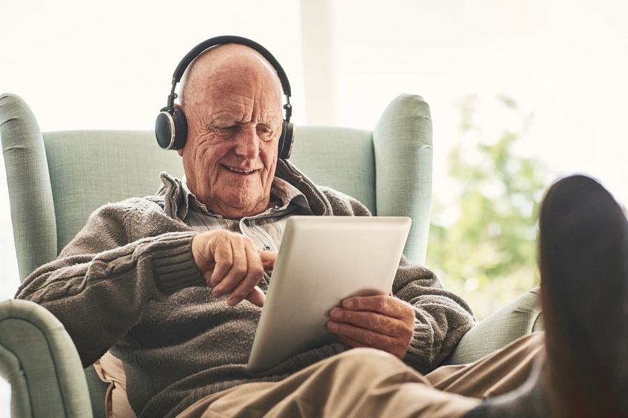 A senior man wearing headphones and using a tablet at home