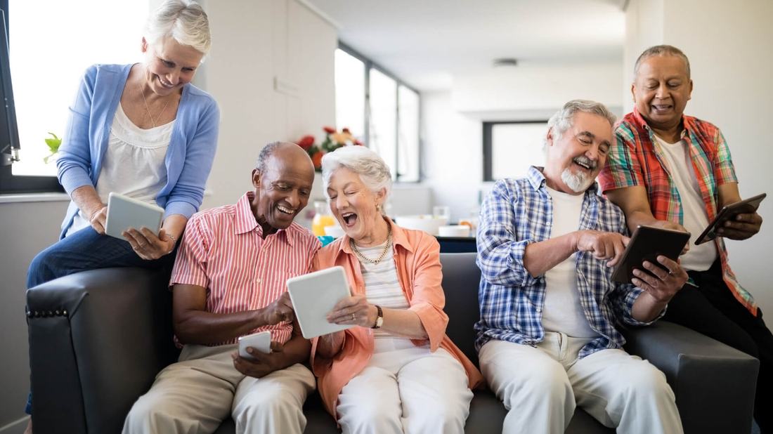 A group of friends laughing together while using tablets and phones