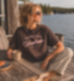 Woman wearing chocolate brown Canadian Huntress t-shirt with soft pink logo near the lake.