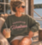 Woman wearing an olive Canadian Huntress crewneck with dusty pink logo sitting at a lakeside cottage dock.