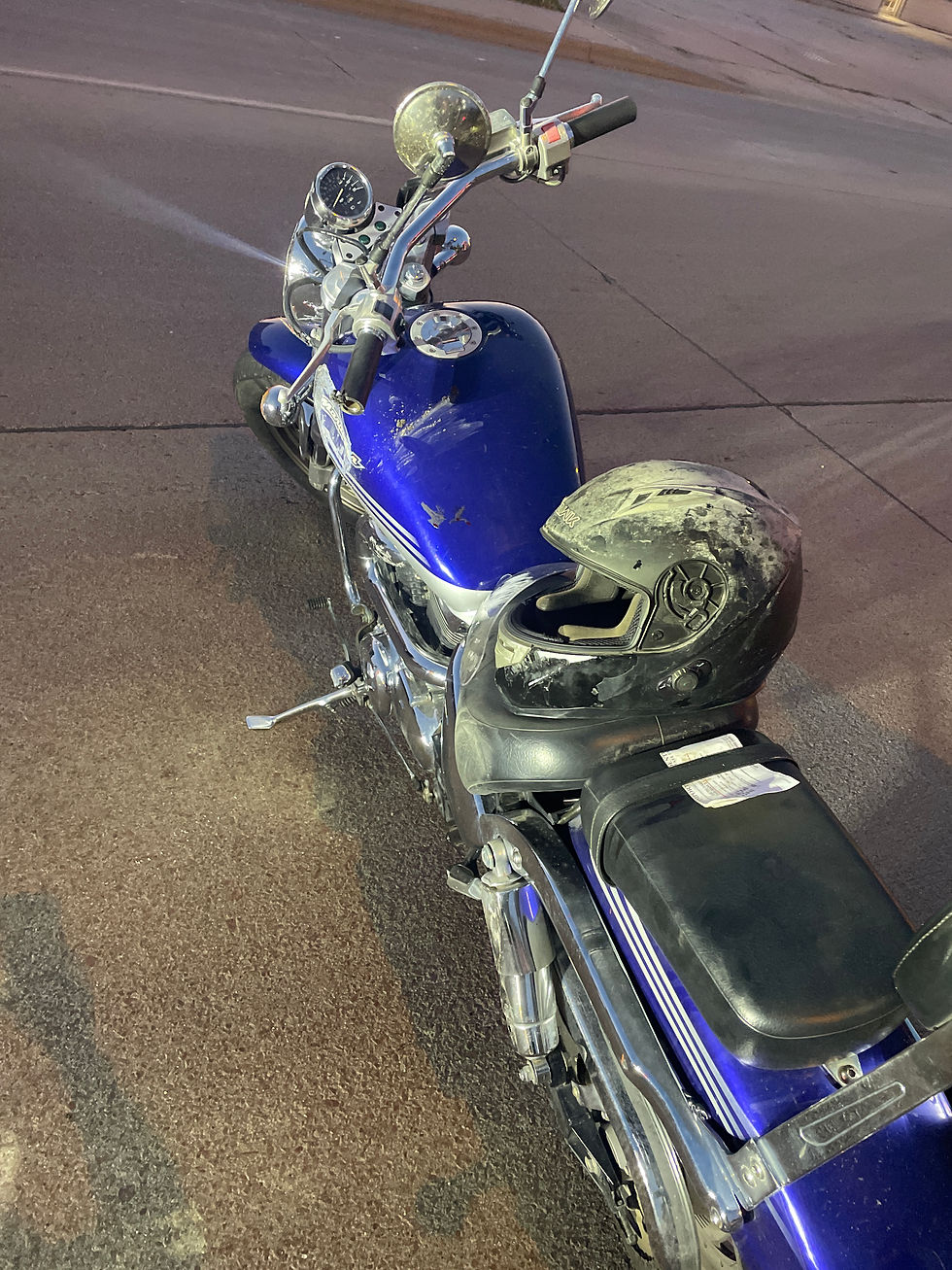 Blue motorcycle parked on cracked pavement with a scuffed black helmet on the seat, evening light reflecting off chrome.