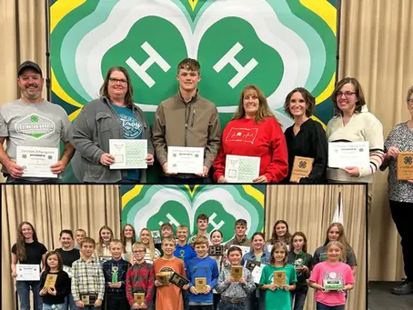 Adults and children proudly hold certificates and plaques in front of a green 4-H banner. Joyful group setting with visible "Northeast Radio SD" logo.