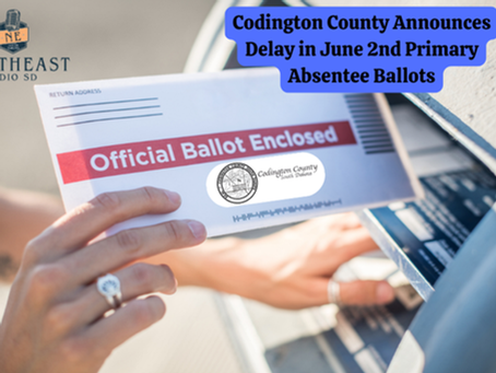 A hand places an "Official Ballot Enclosed" envelope into a mailbox. Text reads "Codington County Announces Delay in June 2nd Primary Absentee Ballots."