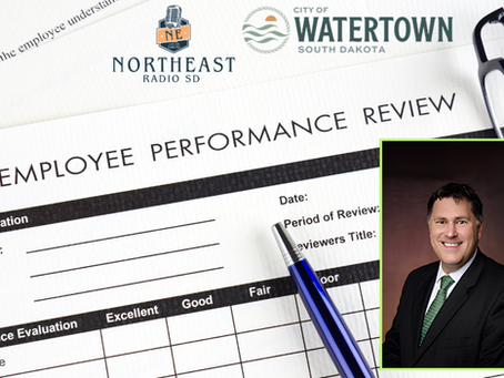 Employee performance review form with Watertown South Dakota and Northeast Radio SD logos, blue pen, glasses, and a smiling portrait.