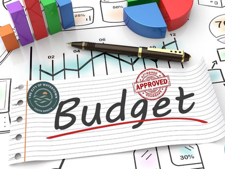 Notepad with "Budget" text and an "Approved" stamp, colorful charts in the background, a pen, and logos of Watertown, SD, and Northeast Radio SD.