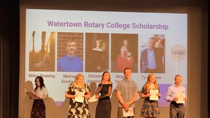 Six people stand on stage holding certificates. A screen reads "Watertown Rotary College Scholarship," with photos and names above.