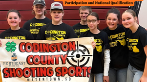 Group of seven smiling teens holding a "Codington County Shooting Sports" banner in a gym. They're wearing black shirts with yellow text.
