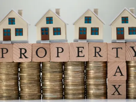 Toy houses on stacked coins spell "PROPERTY TAX" with wooden blocks. Logo in corner reads "NORTHEAST RADIO SD." Neutral background.