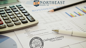 Calculator, pencil, and business charts on desk with Northeast Radio SD and Codington County South Dakota logos; finance planning vibe