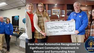 Four people hold a large check for $25,000 at Dave Hahler Automotive. The setting is indoors, with balloons and food in the background.